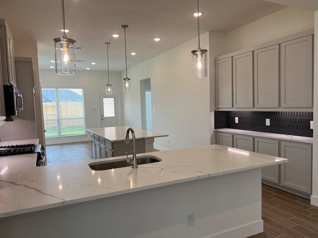kitchen featuring dark wood finished floors, a sink, stainless steel microwave, decorative backsplash, and gray cabinetry