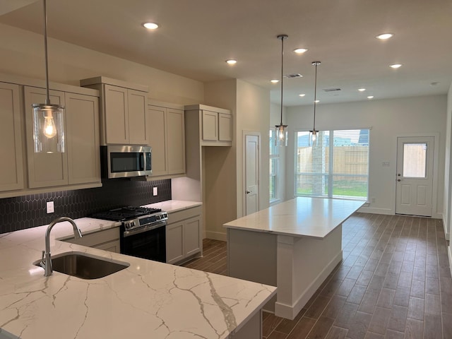 kitchen featuring dark wood-style floors, stainless steel appliances, a sink, a kitchen island, and baseboards