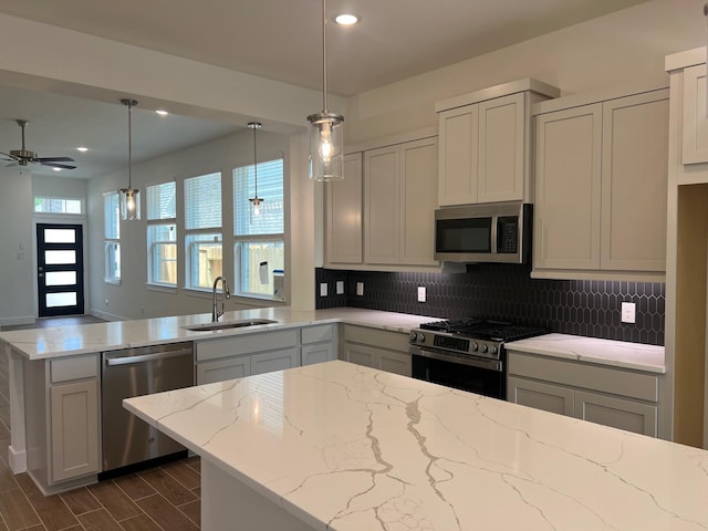 kitchen with light stone counters, a peninsula, appliances with stainless steel finishes, and a sink