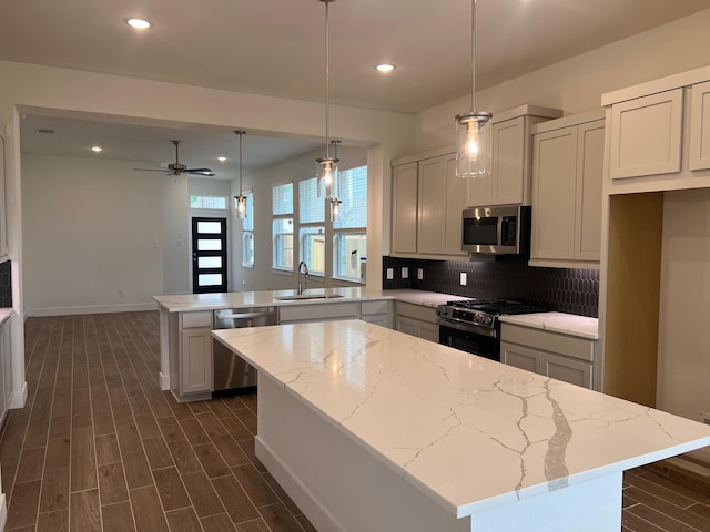 kitchen with dark wood finished floors, stainless steel appliances, a sink, a kitchen island, and a peninsula