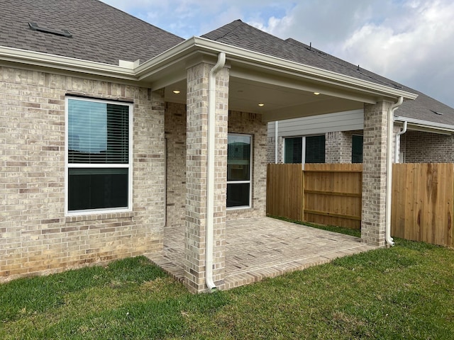 view of home's exterior featuring a shingled roof, a patio, and fence