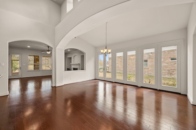 unfurnished living room featuring a towering ceiling, dark hardwood / wood-style flooring, and ceiling fan with notable chandelier