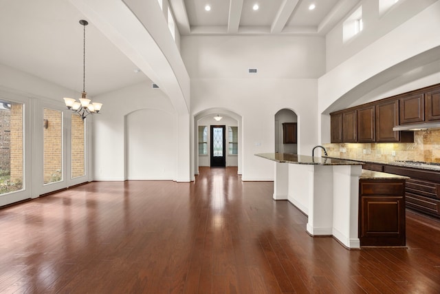 kitchen featuring hanging light fixtures, backsplash, dark hardwood / wood-style floors, dark stone counters, and a chandelier