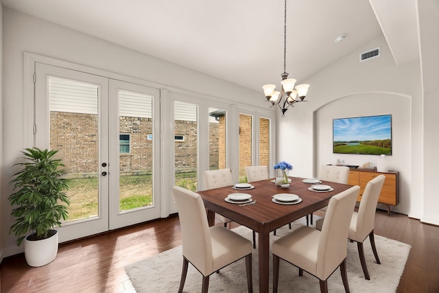 dining space with lofted ceiling, dark hardwood / wood-style floors, an inviting chandelier, and french doors