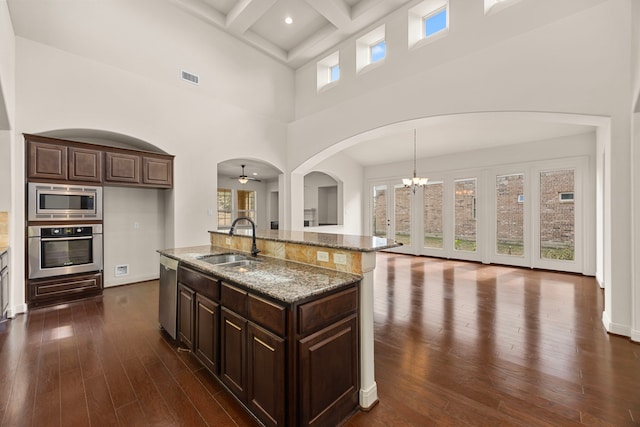 kitchen with sink, stone counters, stainless steel appliances, an island with sink, and decorative light fixtures