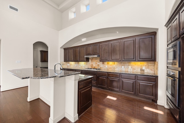 kitchen with a kitchen island with sink, dark brown cabinetry, dark stone counters, and appliances with stainless steel finishes