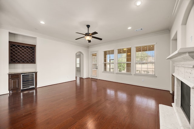 unfurnished living room featuring crown molding, a premium fireplace, dark hardwood / wood-style floors, bar area, and beverage cooler