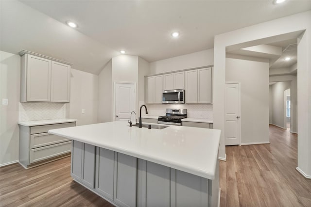 kitchen featuring stainless steel appliances, gray cabinets, sink, and a center island with sink