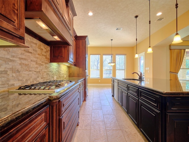 kitchen featuring sink, stainless steel appliances, tasteful backsplash, custom range hood, and decorative light fixtures