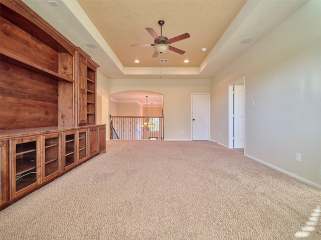 unfurnished living room featuring a tray ceiling, ceiling fan with notable chandelier, and carpet