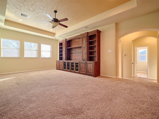 unfurnished living room featuring a tray ceiling, light carpet, and a textured ceiling