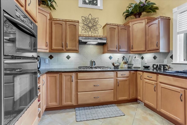 kitchen with light tile patterned flooring, stainless steel gas cooktop, dark stone countertops, double oven, and backsplash