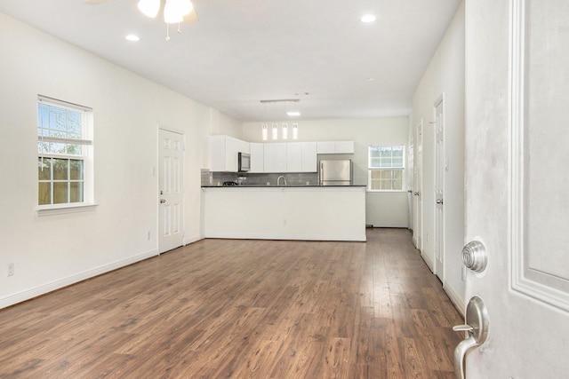 kitchen featuring tasteful backsplash, wood-type flooring, stainless steel fridge, white cabinets, and kitchen peninsula