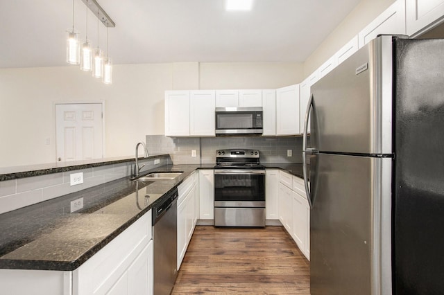 kitchen with sink, decorative light fixtures, dark stone countertops, stainless steel appliances, and white cabinets