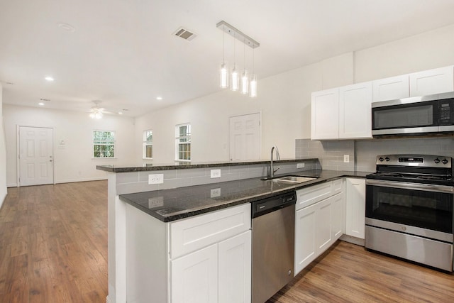 kitchen with appliances with stainless steel finishes, kitchen peninsula, sink, and white cabinets