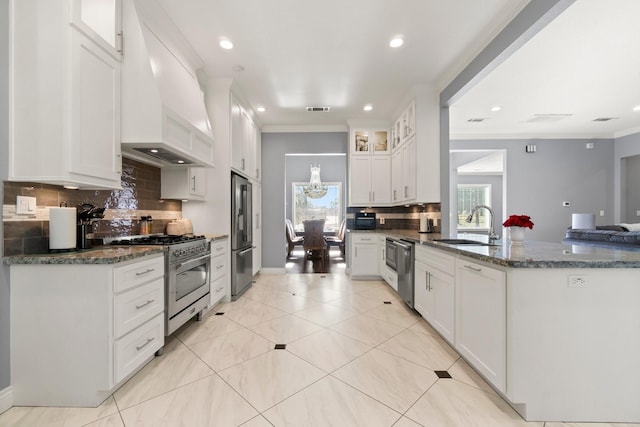 kitchen with crown molding, dark stone countertops, high quality appliances, custom range hood, and white cabinets