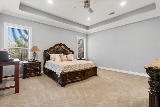 carpeted bedroom featuring ceiling fan, a raised ceiling, and multiple windows