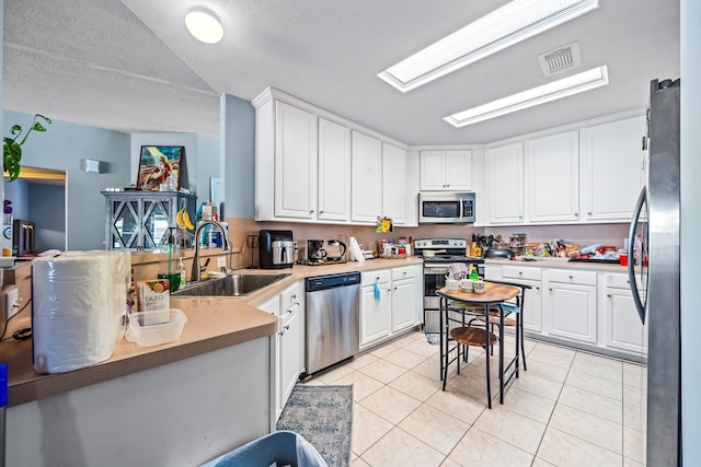 kitchen featuring sink, white cabinetry, a skylight, light tile patterned floors, and appliances with stainless steel finishes