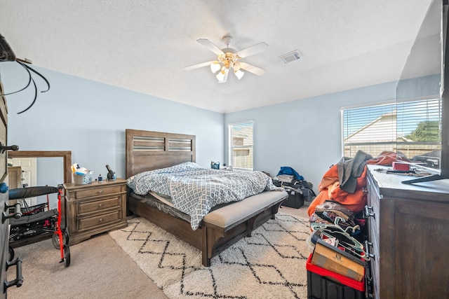 bedroom with multiple windows, ceiling fan, light carpet, and a textured ceiling