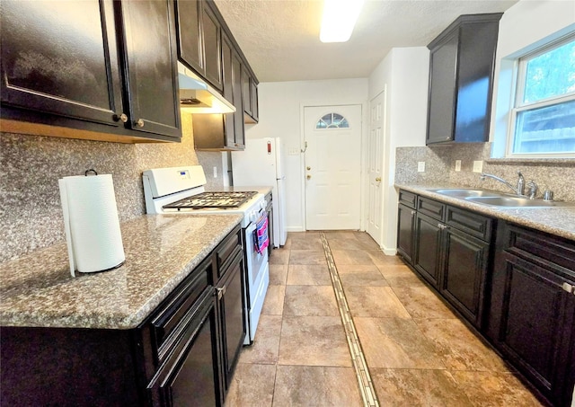 kitchen with sink, backsplash, white appliances, light stone counters, and a textured ceiling