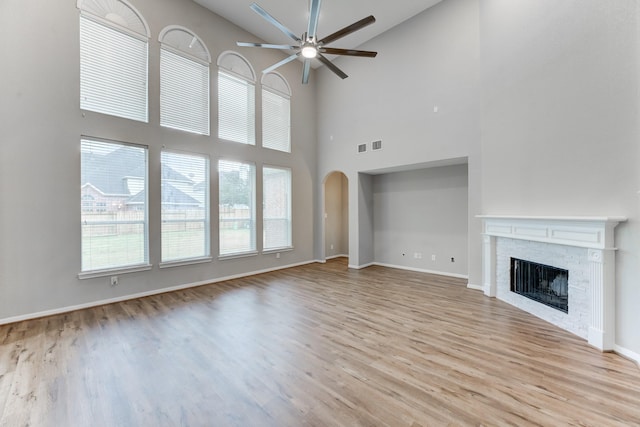 unfurnished living room with ceiling fan, a brick fireplace, and light wood-type flooring