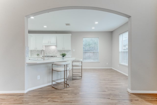 kitchen featuring sink, a kitchen breakfast bar, white cabinets, decorative backsplash, and light wood-type flooring