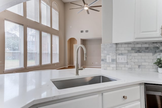 kitchen featuring sink, white cabinets, ceiling fan, light stone countertops, and backsplash