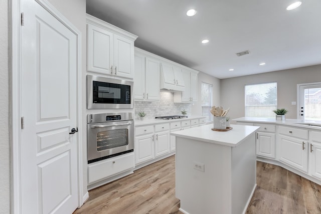 kitchen with white cabinetry, stainless steel appliances, a kitchen island, and light hardwood / wood-style flooring