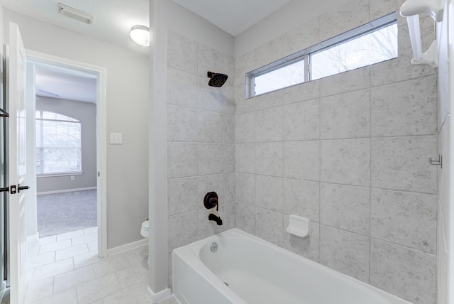 bathroom with toilet, tiled shower / bath combo, and tile patterned flooring