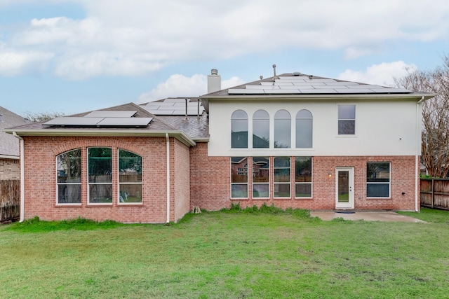 back of property with solar panels, a patio, and a lawn