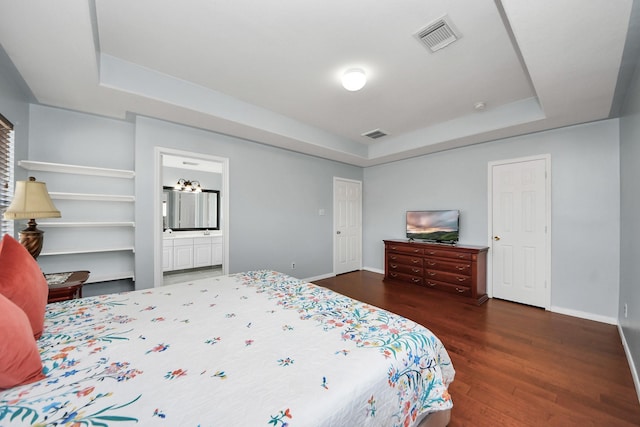 bedroom featuring a raised ceiling, ensuite bathroom, and dark wood-type flooring