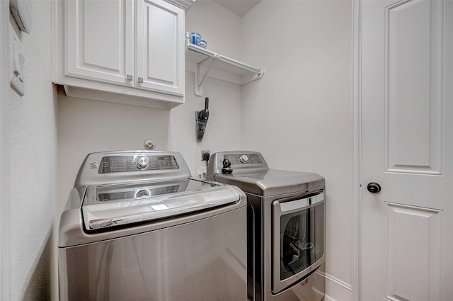 clothes washing area with separate washer and dryer and cabinets