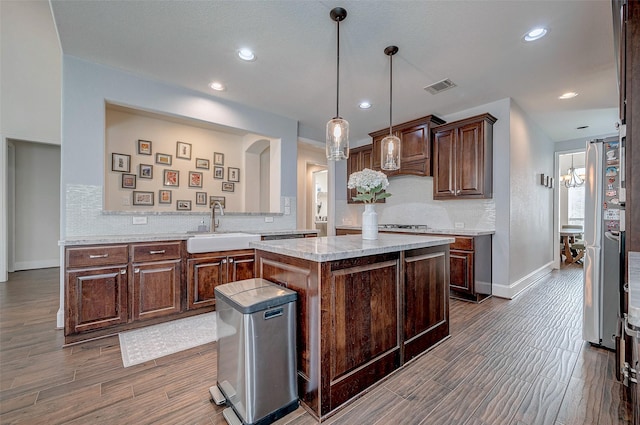 kitchen with tasteful backsplash, dark wood-type flooring, decorative light fixtures, a kitchen island, and sink