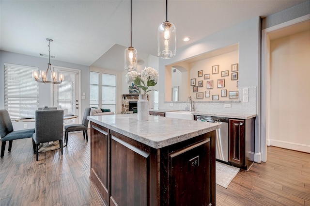 kitchen with light wood-type flooring, sink, stainless steel dishwasher, and decorative light fixtures