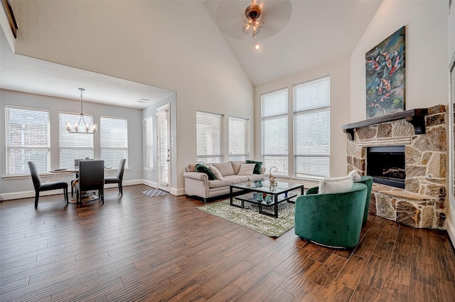 living room featuring a stone fireplace, plenty of natural light, a notable chandelier, and dark hardwood / wood-style flooring