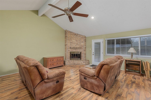 living room with lofted ceiling with beams, hardwood / wood-style flooring, ceiling fan, a brick fireplace, and a textured ceiling