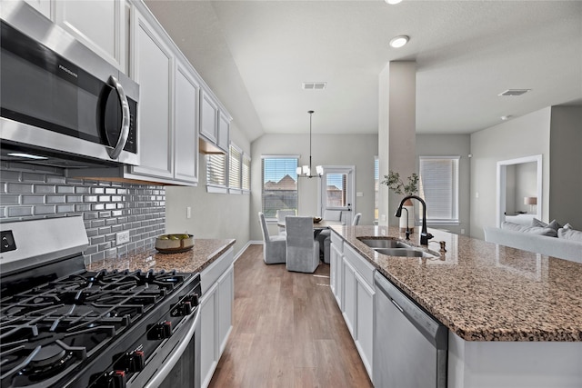 kitchen with sink, white cabinetry, hanging light fixtures, dark stone countertops, and appliances with stainless steel finishes