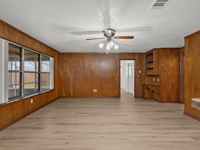 unfurnished living room featuring wood walls, a textured ceiling, and light wood-type flooring