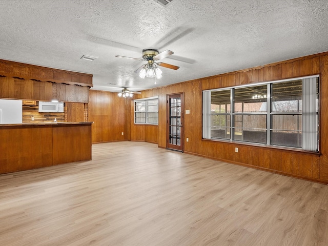 unfurnished living room with wooden walls, a textured ceiling, ceiling fan, and light hardwood / wood-style flooring