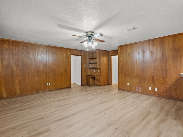 unfurnished living room featuring ceiling fan, wood walls, a textured ceiling, and light wood-type flooring