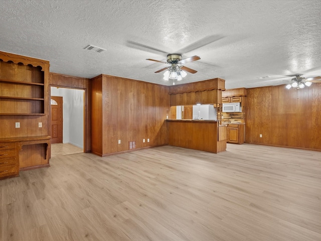 unfurnished living room featuring ceiling fan, built in desk, light wood-type flooring, and wood walls