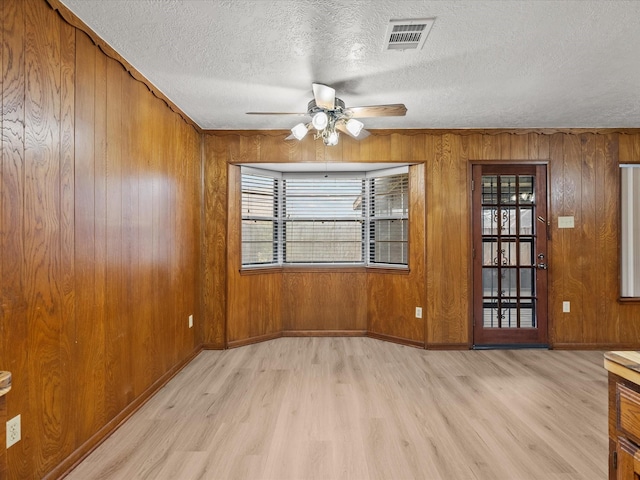 empty room featuring ceiling fan, wooden walls, light hardwood / wood-style floors, and a textured ceiling