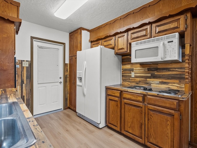 kitchen featuring sink, white appliances, light hardwood / wood-style floors, and a textured ceiling