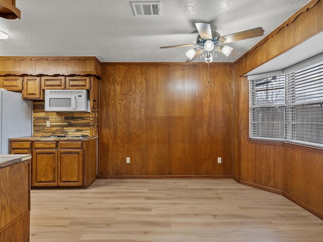 kitchen with wooden walls, white appliances, ceiling fan, light hardwood / wood-style floors, and a textured ceiling