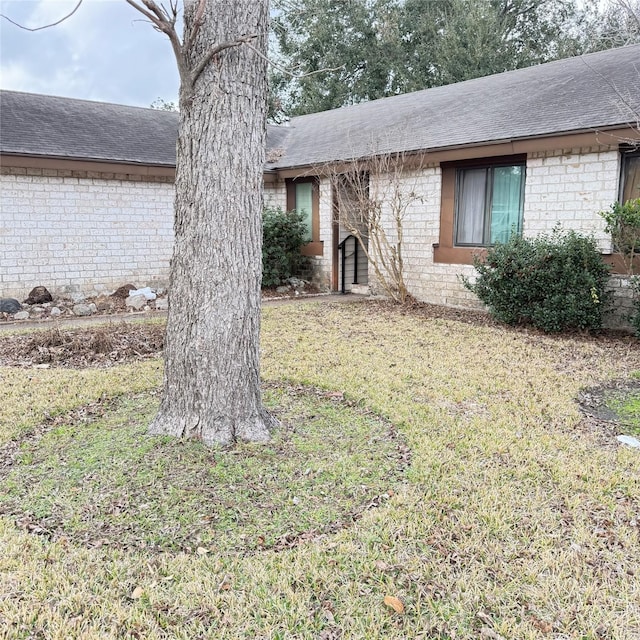 ranch-style home with a front lawn, roof with shingles, and brick siding