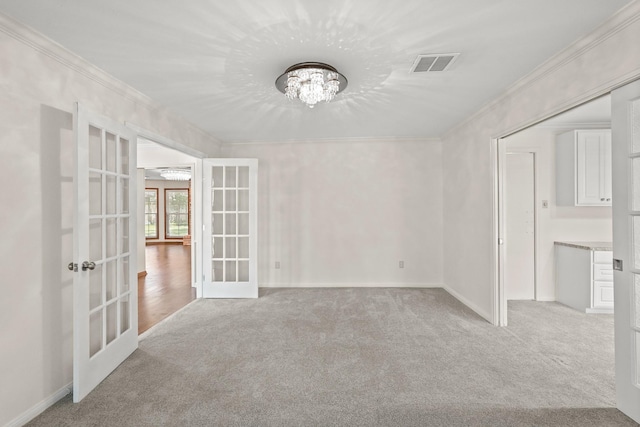 empty room featuring light colored carpet, ornamental molding, french doors, and a chandelier