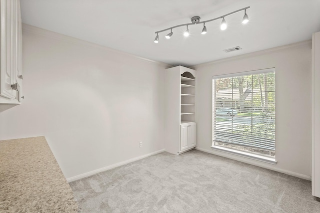 empty room with crown molding, rail lighting, and light carpet