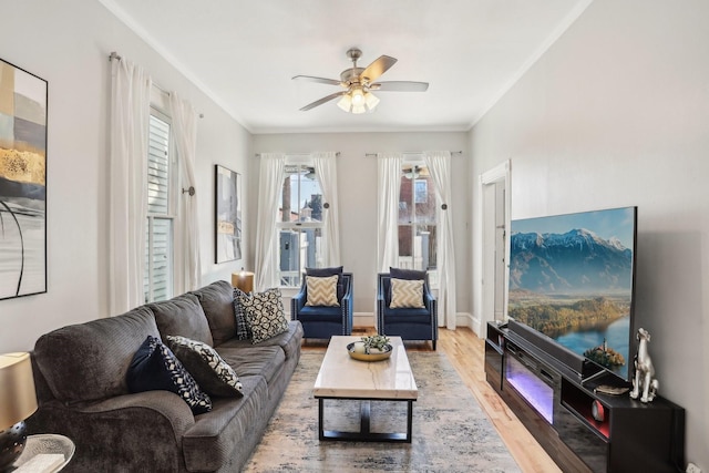 living area with ornamental molding, ceiling fan, baseboards, and wood finished floors