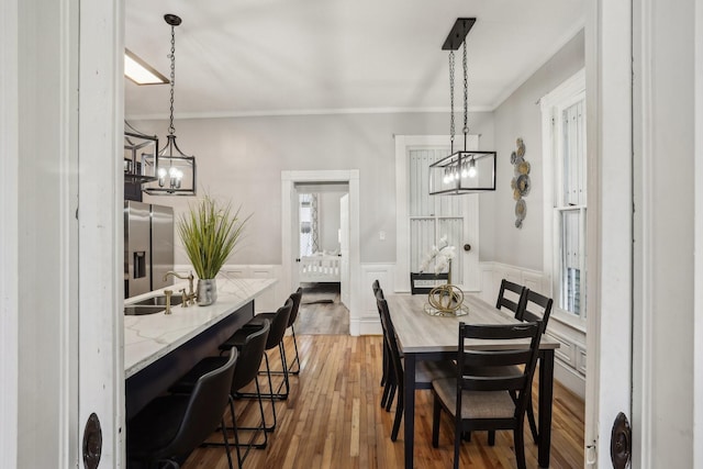 dining space with a decorative wall, an inviting chandelier, ornamental molding, wainscoting, and wood finished floors