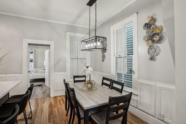 dining space with a wainscoted wall, light wood finished floors, plenty of natural light, and crown molding